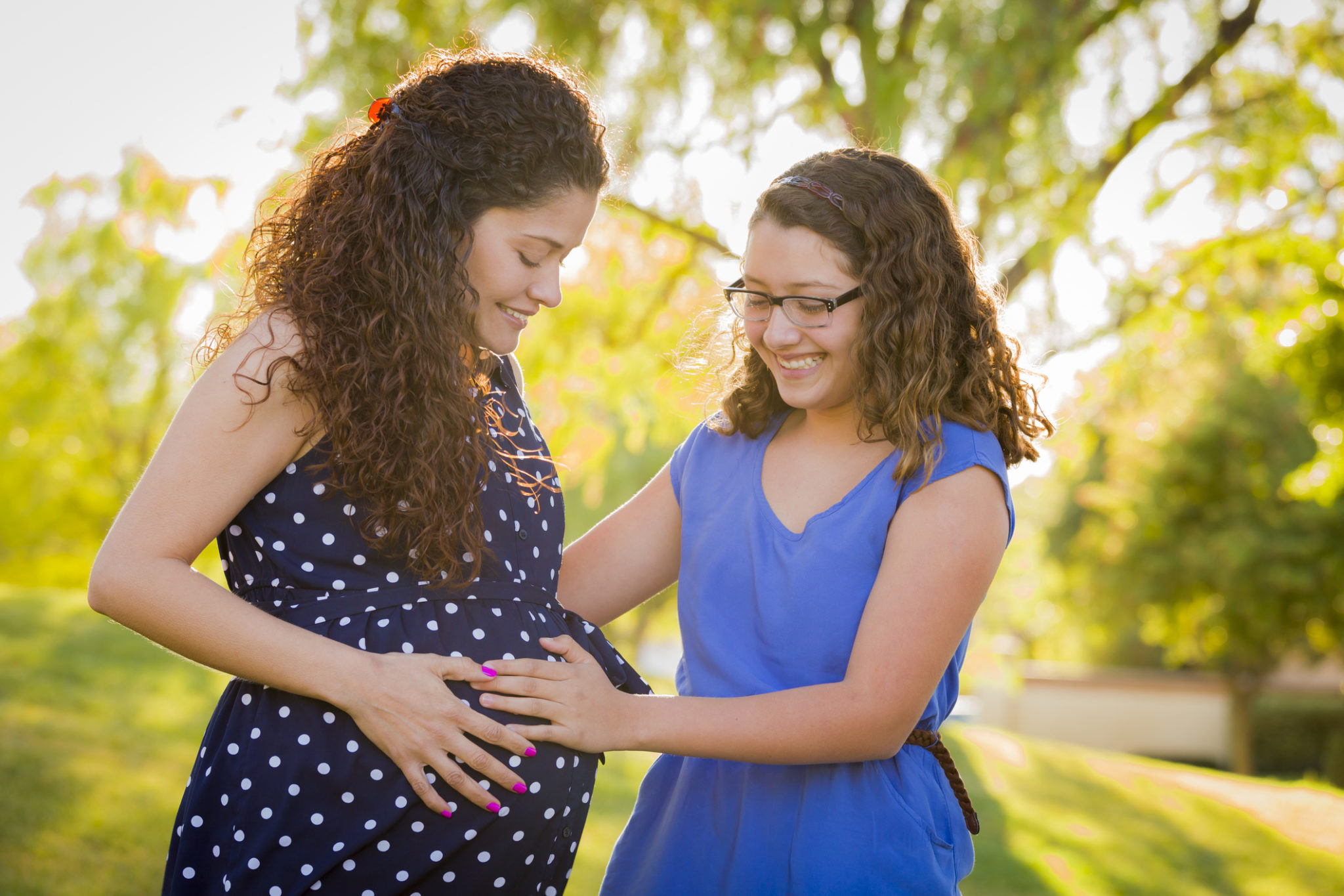 Hispanic Daughter Feels Baby Kick in Pregnant Mother's Tummy Outdoors At the Park.